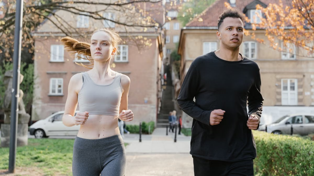 A young woman and man jogging on a city street during the day, wearing sportswear.